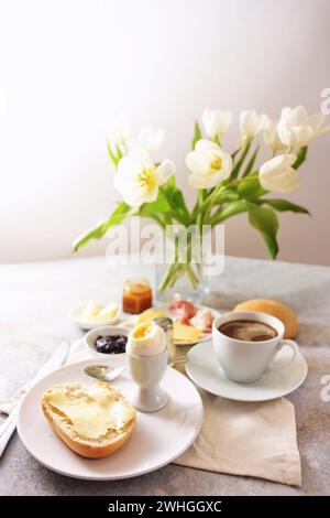 Tavolo per la colazione con fiori, panini, uova cucinate, caffè e molto altro, servito con amore la domenica, il compleanno, la festa della mamma Foto Stock