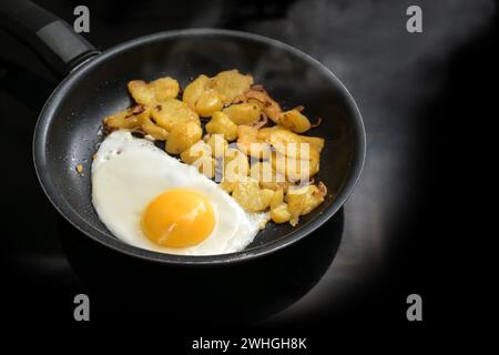 Uova fritte e patate arrosto in una padella nera sul piano cottura in cucina, cottura semplice, spazio per copiare, messa a fuoco selezionata Foto Stock