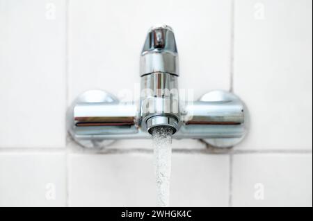 Bagno o rubinetto con acqua corrente su una parete piastrellata bianca in un bagno più vecchio, spazio copia, messa a fuoco selezionata Foto Stock