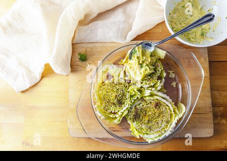 Le fette di cavolo cinese o napa in una casseruola di vetro su una tavola di legno sono ricoperte di spezie e una miscela di formaggio e uova Foto Stock