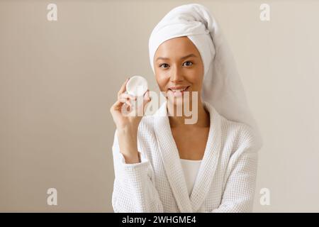 La bella donna con l'abito e l'asciugamano sulla testa pulisce la pelle del suo viso con tamponi di cotone. Pulizia e cura sana del corpo dopo sh Foto Stock