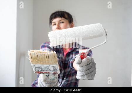 Donna perplessa con rullo per pittura e pittura bianca per pareti in ritratti di primo piano. Lavori di costruzione e riparazioni estetiche in ho Foto Stock