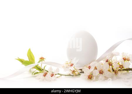 Uovo bianco di Pasqua con un ramo di frutta selvatica in fiore su sfondo chiaro, biglietto d'auguri natalizio, spazio copia, messa a fuoco selezionata Foto Stock