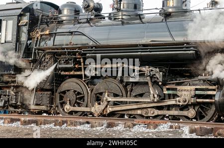 Primo piano di un treno a vapore che esegue l'ingranaggio di comando mentre passa con il vapore che fuoriesce Foto Stock