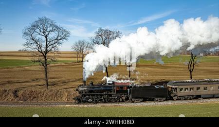 Drone Vista di una locomotiva a vapore in avvicinamento a carrozze passeggeri trainate, soffia fumo bianco Foto Stock