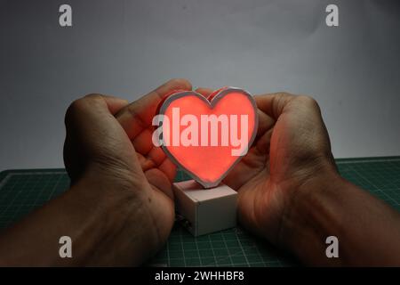 Cuore a LED realizzato utilizzando la tecnologia di stampa 3D coperto di mani che mostra il concetto di amore protetto Foto Stock