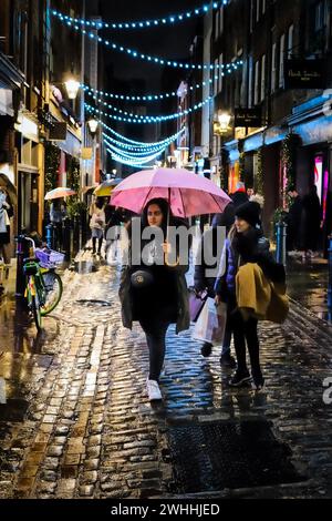 Natale a Covent Garden. Due donne sotto un ombrello sotto la pioggia camminano lungo la strada acciottolata bagnata. Covent Garden a Londra, Regno Unito, il 10 febbraio 2024. Foto di Julie Edwards. Foto Stock