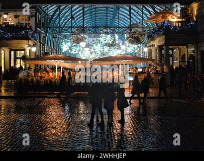 Natale a Covent Garden. Una famiglia si trova sotto un ombrello e ammira le luci del battesimo all'interno del mercato di Covent Garden, mentre le luci si riflettono sulle ciottoli bagnati. Covent Garden a Londra, Regno Unito, il 10 febbraio 2024. Foto di Julie Edwards. Foto Stock