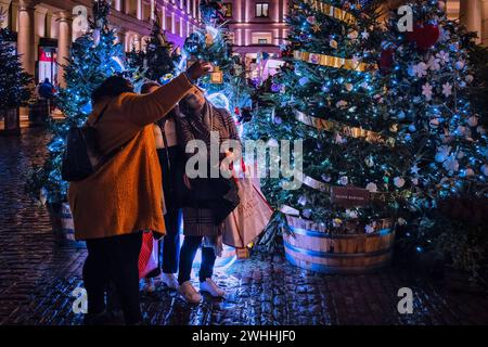 Natale a Covent Garden. 3 persone fanno un selfie di natale davanti agli alberi di Natale. Covent Garden a Londra, Regno Unito, il 10 febbraio 2024. Foto di Julie Edwards. Foto Stock