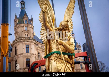 Schwerin, Germania. 8 febbraio 2024. L'Arcangelo Michele viene rimosso dalla cupola d'oro del castello di Schwerin per lavori di restauro utilizzando una gru mobile e caricato su un camion per il trasporto in un'officina. La figura risale al 1857 ed è ufficialmente chiamata "Arcangelo Michele che uccide il drago". L'arcangelo viene ora pulito, restaurato e ridorato in un laboratorio di Berlino prima di tornare al castello in estate. L'Arcangelo Michael Slaying the Dragon è stato restaurato l'ultima volta 30 anni fa. Crediti: Jens Büttner/dpa/Alamy Live News Foto Stock