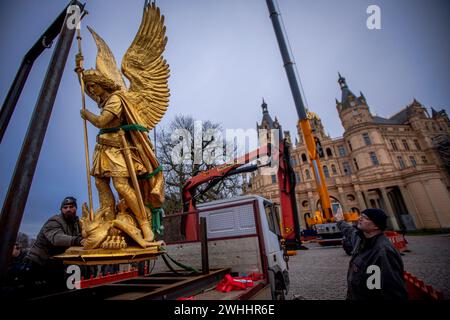 Schwerin, Germania. 8 febbraio 2024. L'Arcangelo Michele viene rimosso dalla cupola d'oro del castello di Schwerin per lavori di restauro utilizzando una gru mobile e caricato su un camion per il trasporto in un'officina. La figura risale al 1857 ed è ufficialmente chiamata "Arcangelo Michele che uccide il drago". L'arcangelo viene ora pulito, restaurato e ridorato in un laboratorio di Berlino prima di tornare al castello in estate. L'Arcangelo Michael Slaying the Dragon è stato restaurato l'ultima volta 30 anni fa. Crediti: Jens Büttner/dpa/Alamy Live News Foto Stock