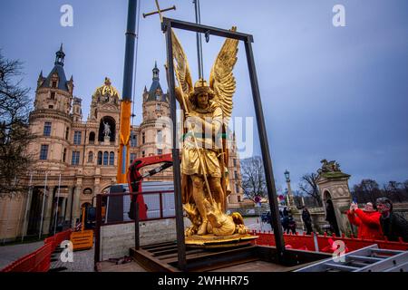 Schwerin, Germania. 8 febbraio 2024. L'Arcangelo Michele viene rimosso dalla cupola d'oro del castello di Schwerin per lavori di restauro utilizzando una gru mobile e caricato su un camion per il trasporto in un'officina. La figura risale al 1857 ed è ufficialmente chiamata "Arcangelo Michele che uccide il drago". L'arcangelo viene ora pulito, restaurato e ridorato in un laboratorio di Berlino prima di tornare al castello in estate. L'Arcangelo Michael Slaying the Dragon è stato restaurato l'ultima volta 30 anni fa. Crediti: Jens Büttner/dpa/Alamy Live News Foto Stock