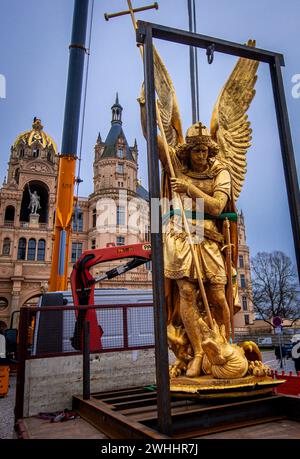 Schwerin, Germania. 8 febbraio 2024. L'Arcangelo Michele viene rimosso dalla cupola d'oro del castello di Schwerin per lavori di restauro utilizzando una gru mobile e caricato su un camion per il trasporto in un'officina. La figura risale al 1857 ed è ufficialmente chiamata "Arcangelo Michele che uccide il drago". L'arcangelo viene ora pulito, restaurato e ridorato in un laboratorio di Berlino prima di tornare al castello in estate. L'Arcangelo Michael Slaying the Dragon è stato restaurato l'ultima volta 30 anni fa. Crediti: Jens Büttner/dpa/Alamy Live News Foto Stock