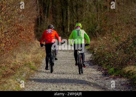 Due persone stanno pedalando lungo un sentiero tra alberi e piante lussureggianti nella foresta, godendo di attività ricreative all'aperto sulle loro biciclette. Foto Stock