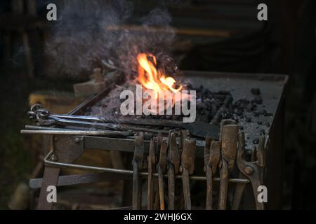 Fucina portatile di fabbro con varie pinze arrugginite e fuoco di carbone in fiamme in uno storico mercato artigianale, spazio copia, selezionato Foto Stock