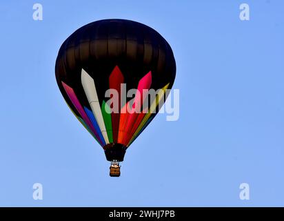Vista di una mongolfiera, nera con strisce colorate che volano in un cielo completamente blu Foto Stock