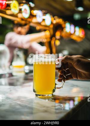 Birra appena spillata. Mano che regge un bicchiere di birra appena spillata. Birra artigianale versata in un bicchiere da pinta. Barman che versa una grande birra lager alla spina Foto Stock