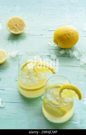 Limonata. Bere acqua di limone con ghiaccio, due bicchieri e frutta su blu Foto Stock