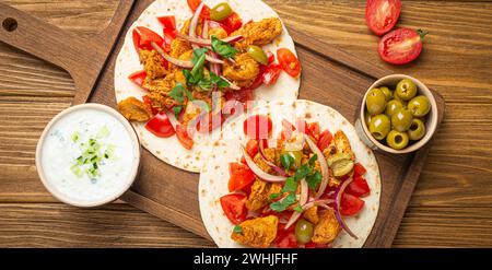 Cucina tradizionale greca Gyros: Pane Pita con verdure, carne, erbe, olive su tagliere rustico di legno con Tzatzi Foto Stock