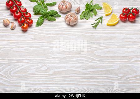 Composizione sana degli ingredienti alimentari con pomodori ciliegini freschi, erbe, spicchi d'aglio, spicchi di limone su dorso di legno bianco Foto Stock