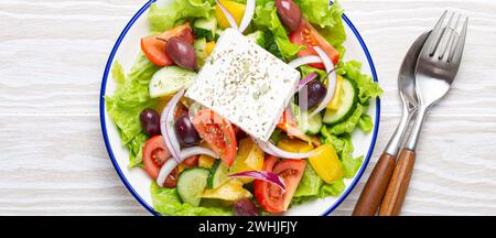 Insalata greca tradizionale con feta, pomodori, peperoni, cetrioli, olive, erbe in un recipiente di ceramica bianca su rustico bianco Foto Stock