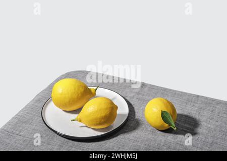 Colori di tendenza del 2021. Limoni illuminanti gialli su tovaglia Ultimate grigia. Vista isometrica minima natura morta Foto Stock