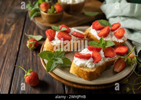 Colazione con toast alle bacche, cibo sano. Sandwich con fragole e formaggio morbido su fondo in legno. Copia spazio. Foto Stock