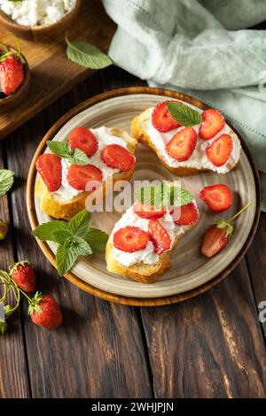 Colazione con toast alle bacche, cibo sano. Sandwich con fragole e formaggio morbido su fondo in legno. Copia spazio. Foto Stock