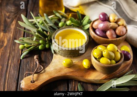 Olive appena raccolte frutti di bosco in ciotole di legno e olio pressato servito su vecchie tavole di legno. Copia spazio. Foto Stock