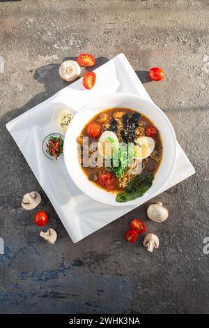 Una gustosa ciotola di ramen con verdure, funghi, uova e spaghetti. Brodo ricco, ricoperto di funghi, pomodori, cipolle verdi. Servito con uova sode e limone Foto Stock