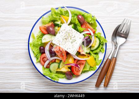 Insalata greca tradizionale con feta, pomodori, peperoni, cetrioli, olive, erbe in un recipiente di ceramica bianca su rustico bianco Foto Stock