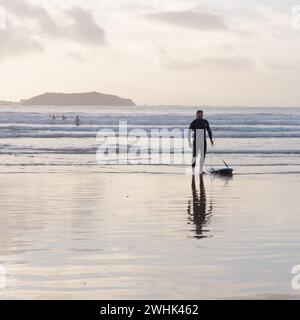 Surfer con Surf Board lascia il mare mentre le persone giocano sulle onde a Essaouira, Marocco. 10 febbraio 2024 Foto Stock