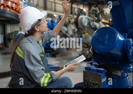 Un ingegnere donna installa un programma su un braccio robotico in un magazzino robot. E provare il funzionamento prima di inviare la macchina Foto Stock