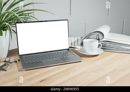 Modella su un computer portatile aperto con schermo bianco vuoto, tazza da caffè e raccoglitore di anelli su una scrivania di legno su una superficie dipinta di bianco Foto Stock