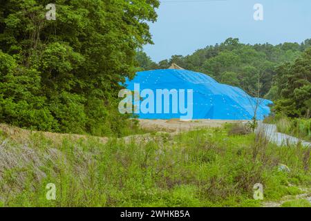 Grande collina di terra del cantiere ricoperta di tela cerata blu in campagna circondata da alberi Foto Stock