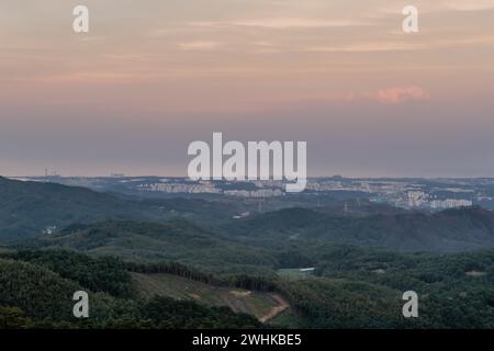 Paesaggio di una grande città sulla costa preso dalla vista delle montagne con strati visibili di copertura nuvolosa sull'oceano blu in lontananza nella Corea del Sud Foto Stock