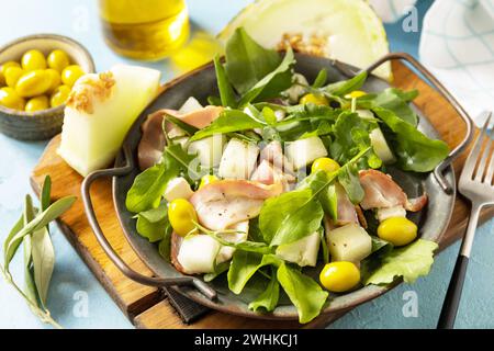 Antipasto tradizionale spagnolo e italiano. Insalata mediterranea estiva con melone, pancetta, olive, formaggio bianco e rucola in blu Foto Stock