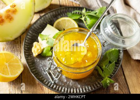 Marmellata di melone dolce e agrumi o gelatina in piccolo vaso di vetro con fette di melone fresche su tavola rustica in legno. Conserva fatta in casa. Foto Stock