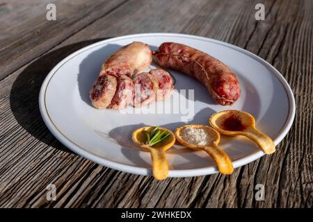 Un piatto con salsiccia Luganighe e con specie a cucchiaio come zafferano e parmigiano e rosmarino su un piatto su un tavolo di legno con luce solare Foto Stock