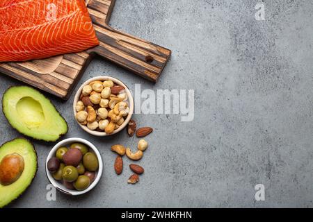 Fonti alimentari di grassi insaturi sani e omega 3: Filetto di salmone crudo fresco, avocado, olive, noci su tagliere, frutta secca rustica Foto Stock