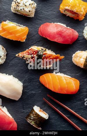 Sushi con bacchette, colpo in alto. Rotoli, maki, nigiri su sfondo nero Foto Stock