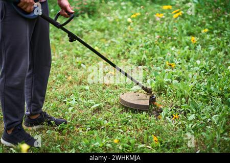 Primo piano di un giovane che taglia l'erba con il taglierine sul suo prato erboso. Foto Stock