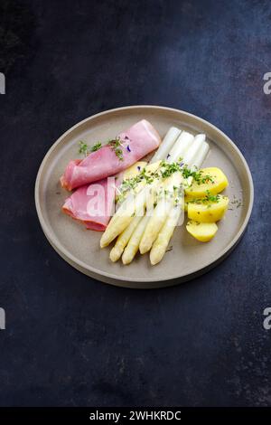 Asparagi bianchi al vapore tradizionali con prosciutto di ginepro e patate bollite in salsa hollandaise serviti come primo piano su un pla di design Foto Stock