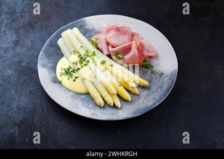 Asparagi bianchi al vapore tradizionali con prosciutto di ginepro e salsa hollandaise serviti da primo piano su un piatto di design Foto Stock