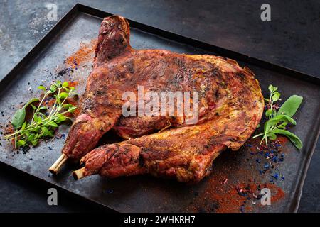 Tradizionale barbeque metà di capra da latte con spalle e gambe servito come primo piano su un vassoio nero rustico Foto Stock