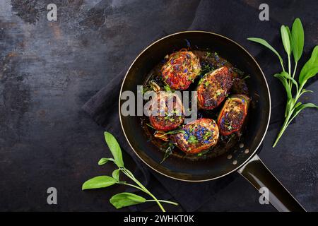 Tradizionali medaglioni di filetto di vitello arrosto con rivestimento di pancetta e foglie di salvia in salsa di burro serviti come vista dall'alto su un battuto rustico Foto Stock