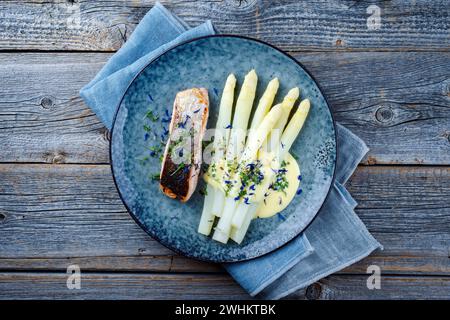 Asparagi bianchi cotti al vapore tradizionali con filetto di salmone e salsa hollandaise serviti come vista dall'alto su un piatto di design con copia spac Foto Stock