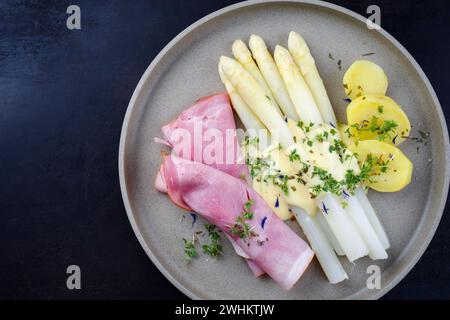 Asparagi bianchi al vapore tradizionali con prosciutto di ginepro e patate bollite in salsa hollandaise serviti come vista dall'alto su un pla di design Foto Stock