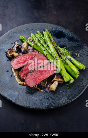 Bistecca di manzo angus stagionato al barbecue gourmet con asparagi verdi e funghi in mousse al tartufo parfait e salsa di ciliegie selvatiche Foto Stock