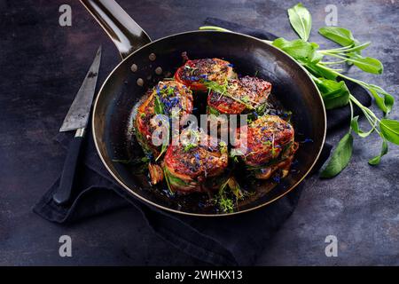 Tradizionali medaglioni di filetto di vitello arrosto con rivestimento di pancetta e foglie di salvia in salsa di burro serviti da vicino su un battuto rustico Foto Stock